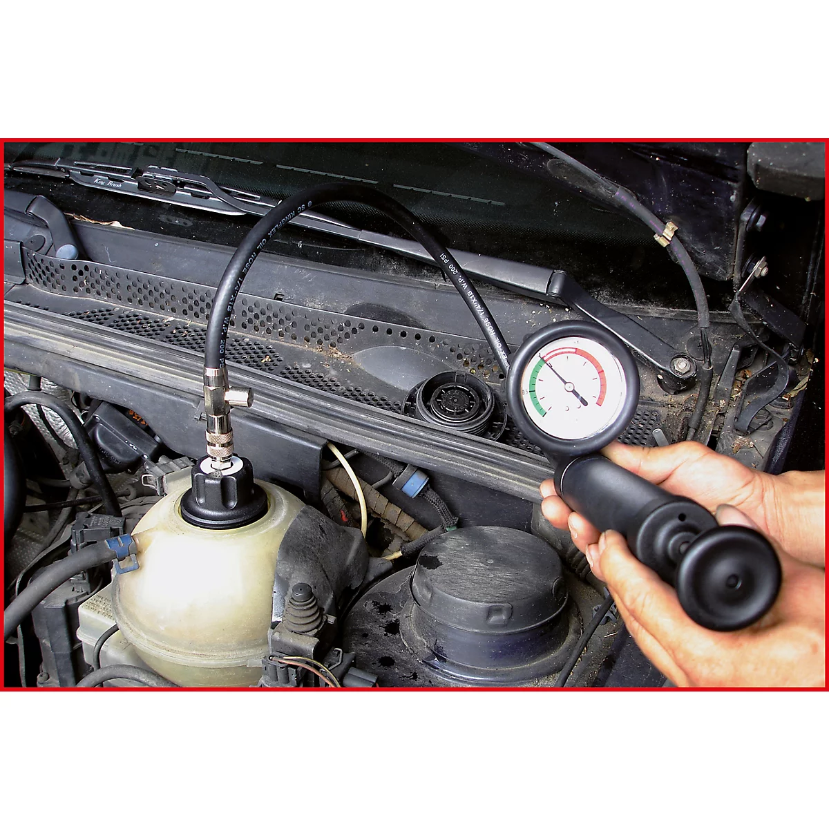 Ein Mann prüft den Kühlmittelstand in einem Motorraum mit einem Manometer. Das Messgerät zeigt grünen Bereich an.